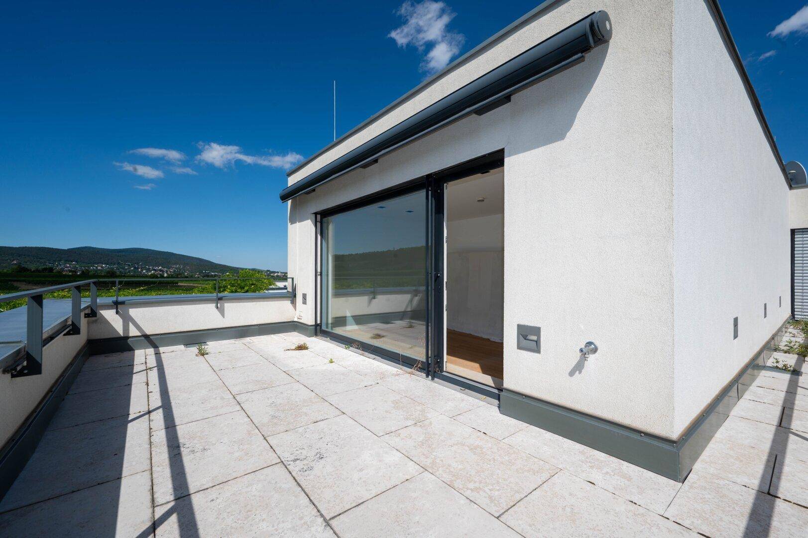 Geräumige Dachterrasse mit Fliesenboden, Markise und weitem Blick auf die umliegende Landschaft.