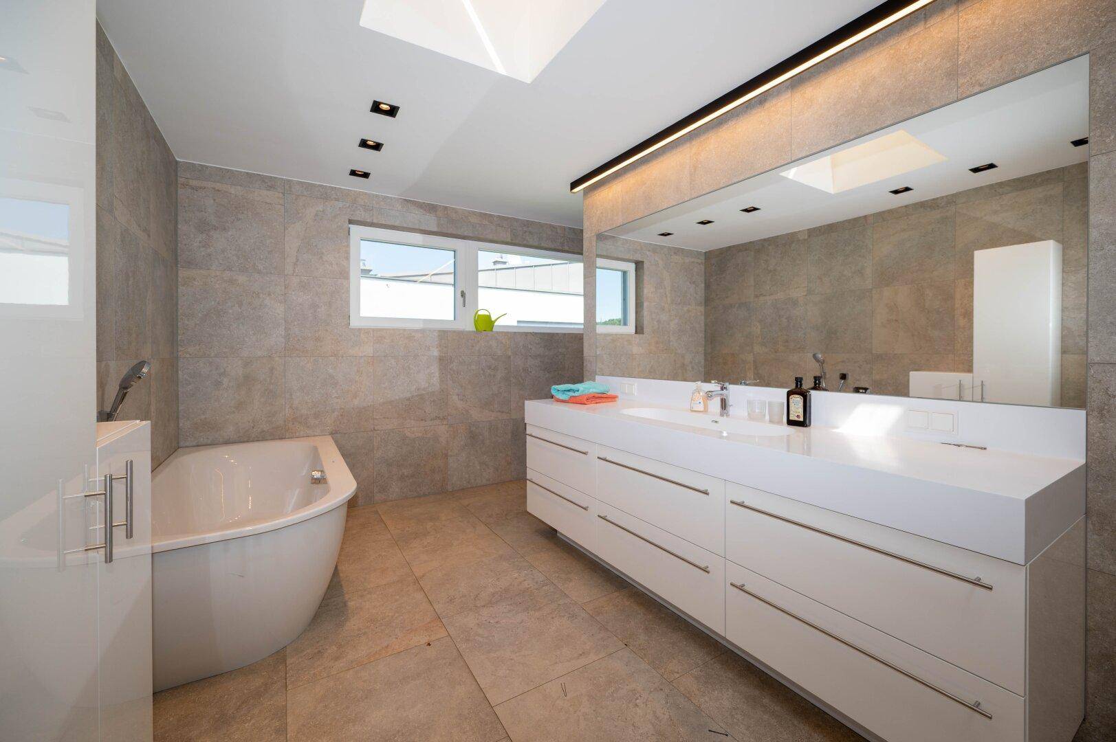 Modernes Badezimmer mit großer Badewanne, Doppelwaschbecken und Oberlicht für viel Licht.