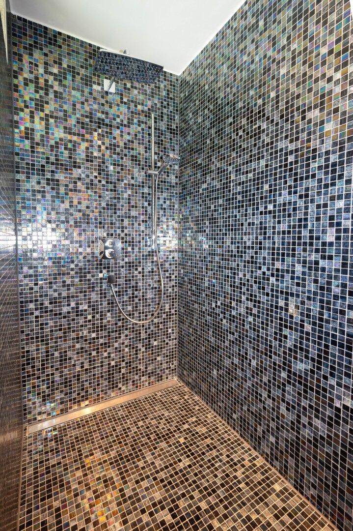 Moderne Duschkabine mit farbigen Mosaikfliesen und Regendusche, stilvoll gestaltet.