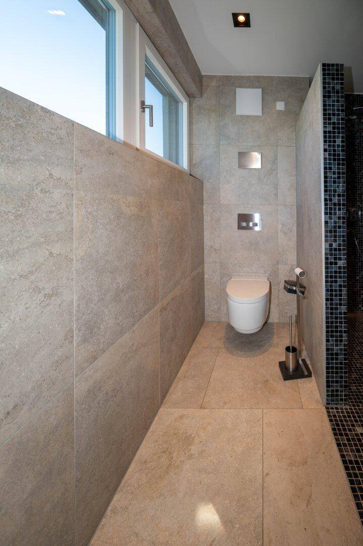 Modernes WC mit Wandtoilette und großen Fliesen, hell und funktional.