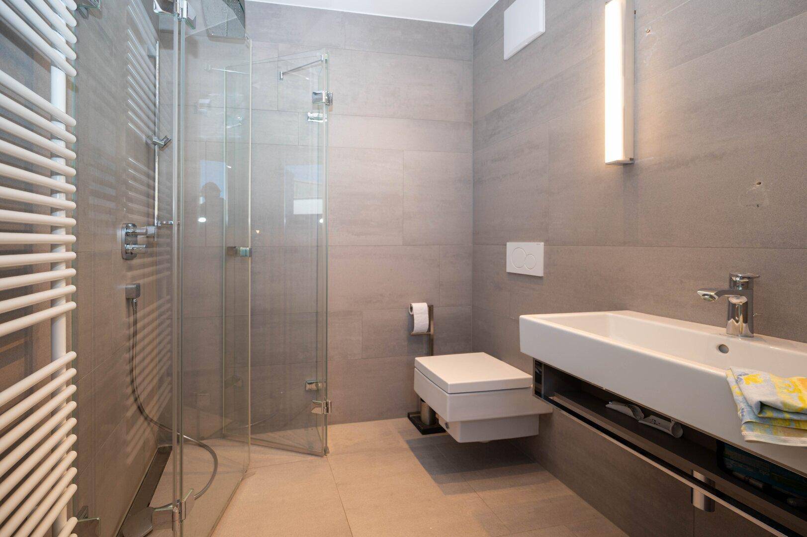 Modernes Badezimmer mit Duschkabine, Waschbecken und beheiztem Handtuchhalter.