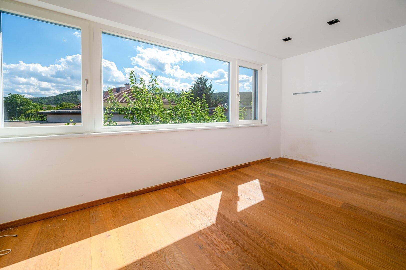 Heller Raum mit Holzboden und großen Fenstern, die viel Tageslicht hereinlassen.