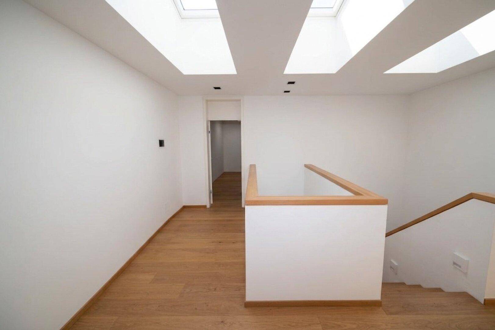 Heller Flur mit Holztreppe, Parkettboden und Oberlichtern, der zu weiteren Etagen führt.