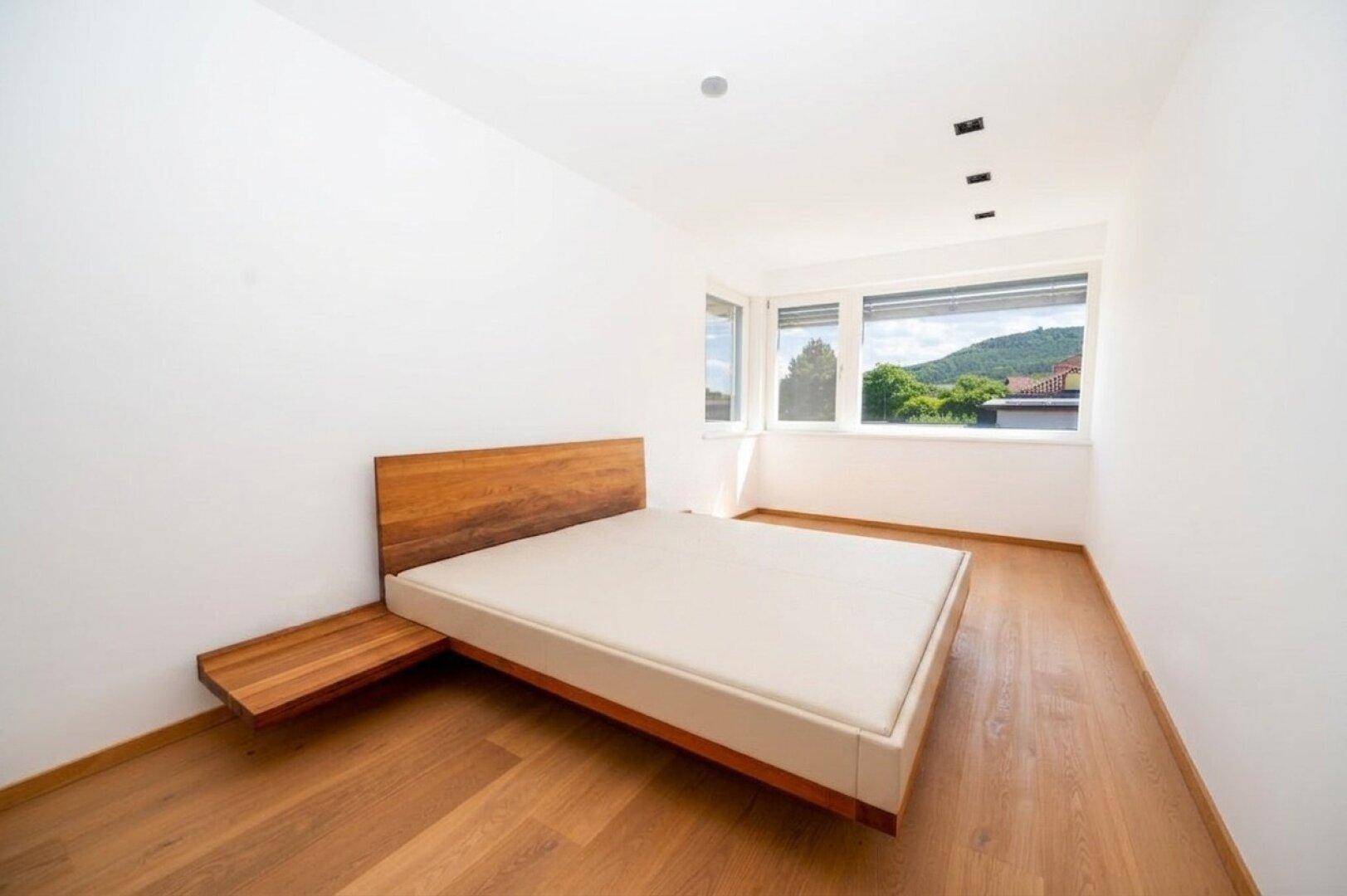 Helles Schlafzimmer mit Holzboden und modernem Bett, großer Fensterfront mit Ausblick.