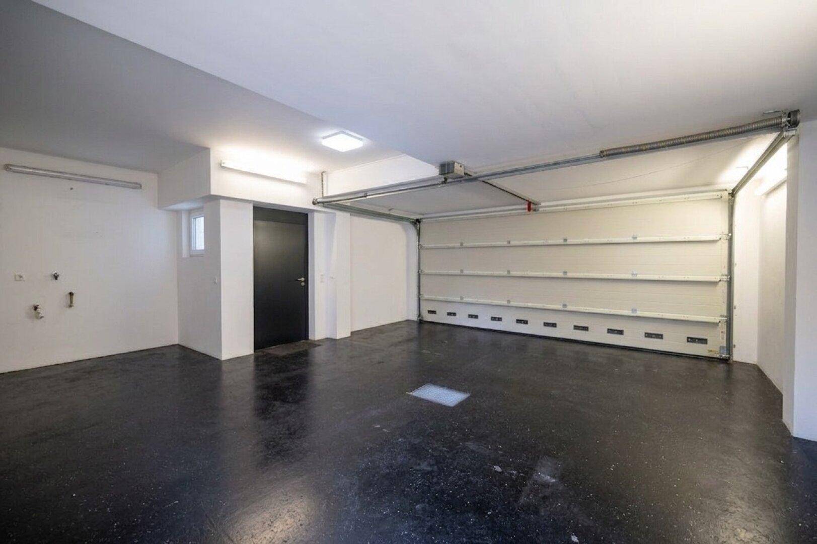 Leere Garage mit automatischem Garagentor und dunklem Boden.