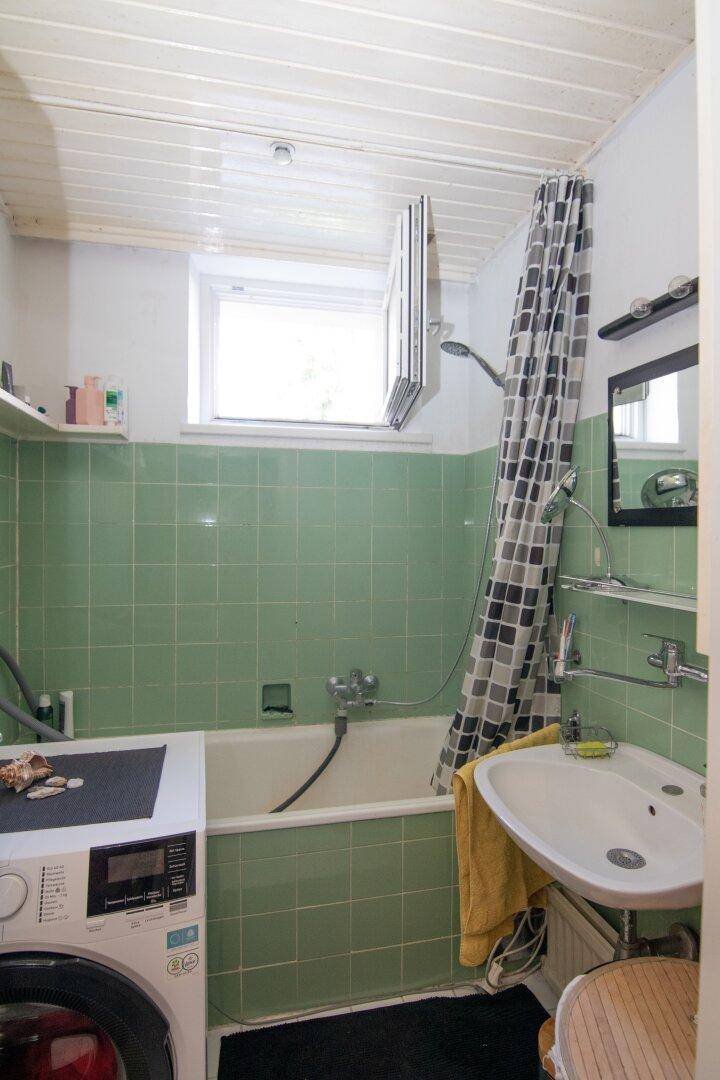 Badezimmer mit grünen Fliesen, Badewanne mit Duschvorhang und Waschmaschine.