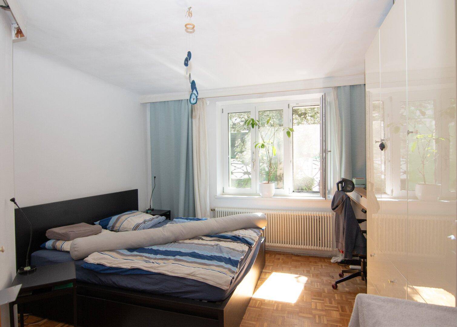 Schlafzimmer mit Doppelbett, Schreibtisch und großem Fenster, das viel Tageslicht bietet.
