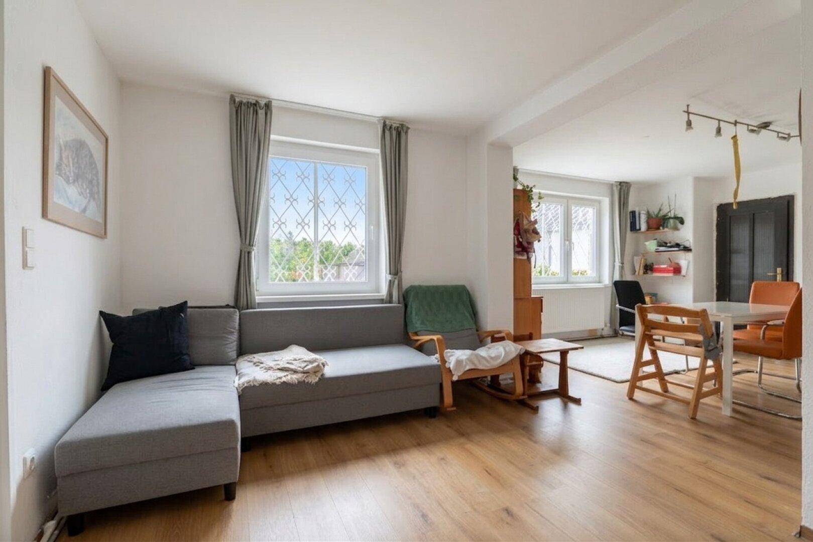 Heller Wohn- und Essbereich mit Holzfußboden, gemütlichem Sofa und Blick ins Grüne.
