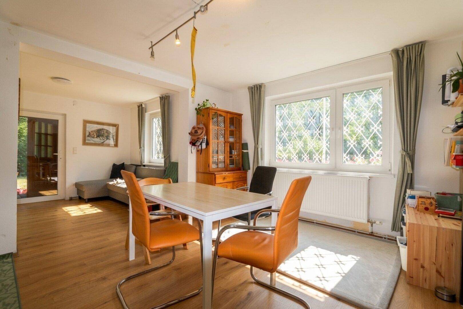 Geräumiger Essbereich mit Holztisch und Stühlen, offen zum Wohnzimmer mit großen Fenstern.