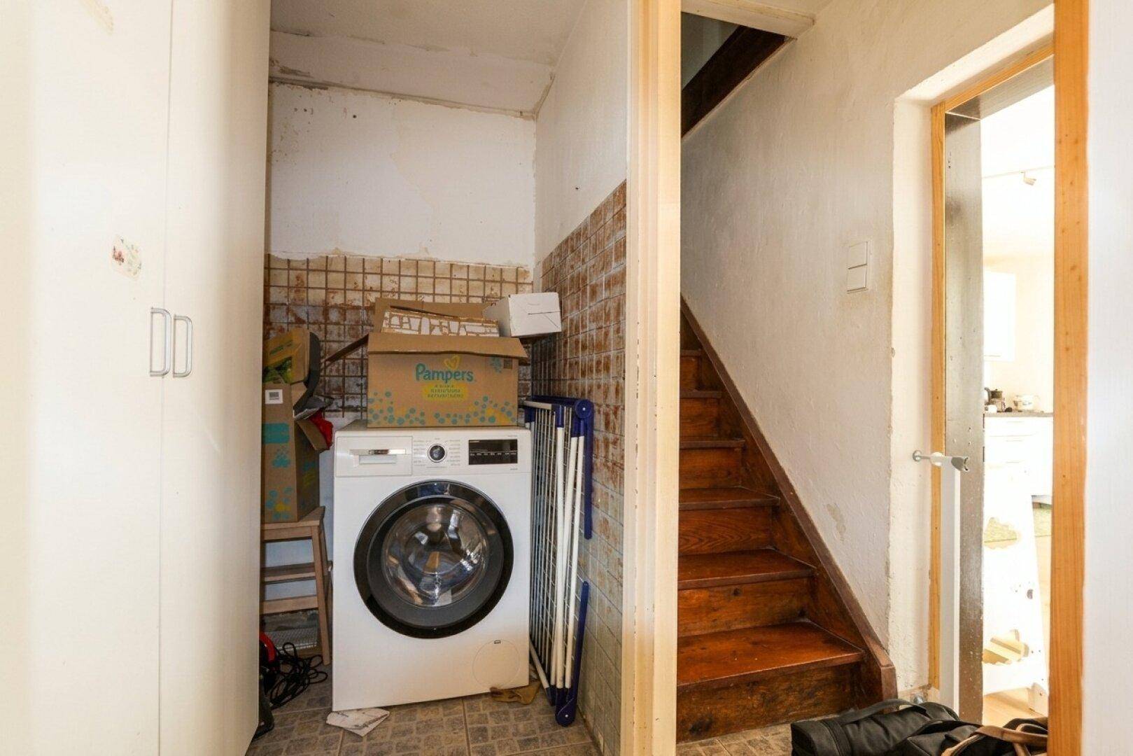 Praktischer Hauswirtschaftsraum mit Waschmaschine und Zugang zur Holztreppe.