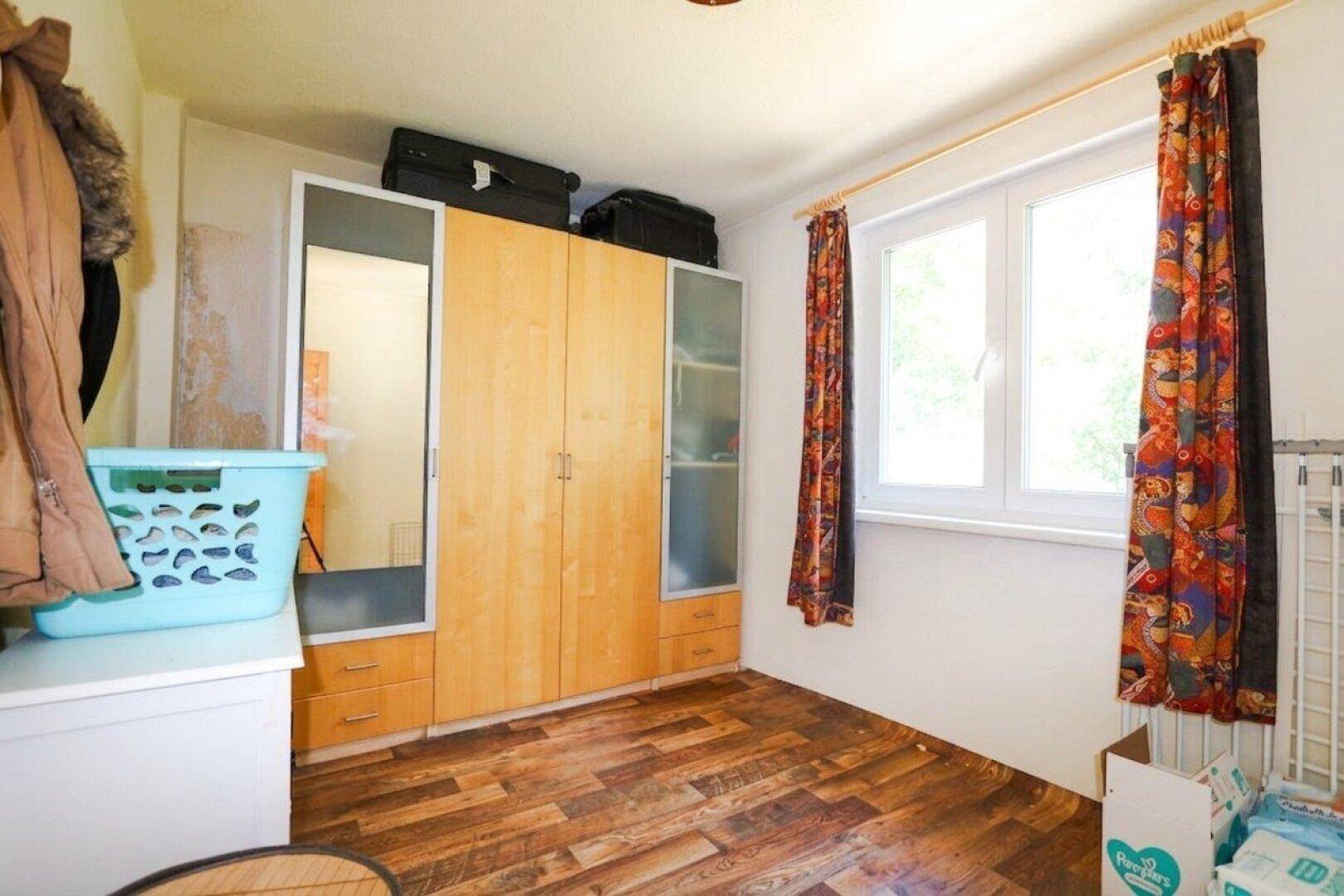 Schlafzimmer mit großem Kleiderschrank und Holzfußboden, gut beleuchtet durch ein Fenster.
