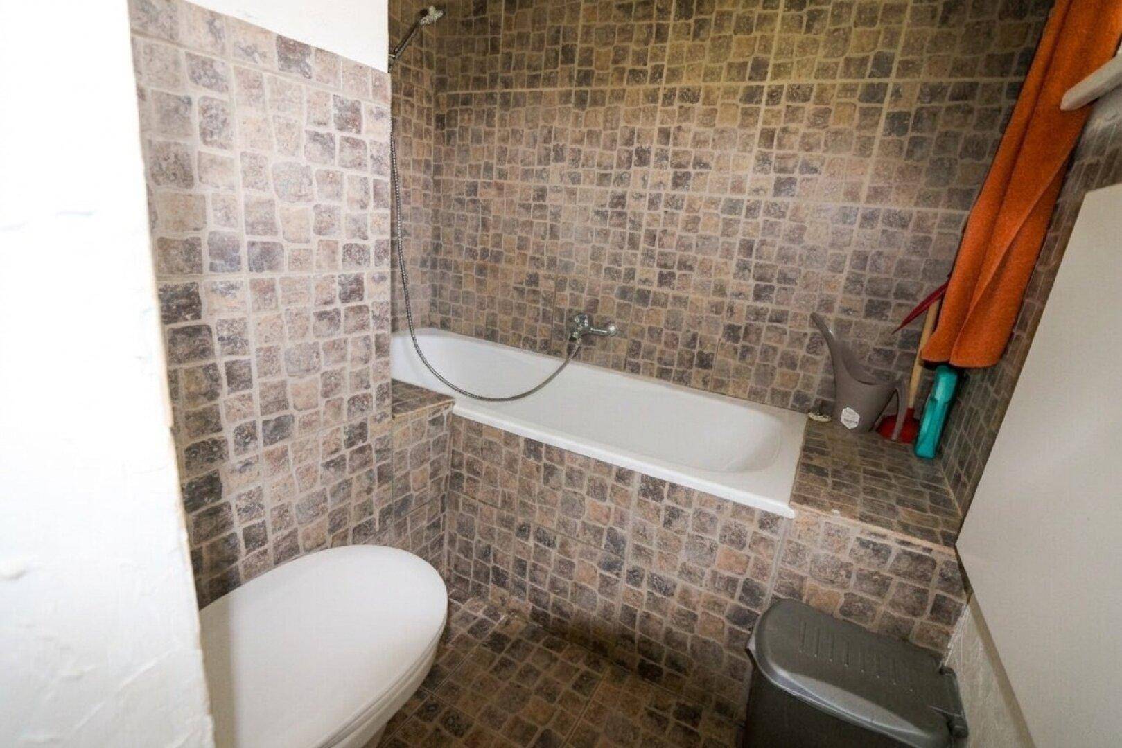 Badezimmer mit Badewanne und Toilette, gefliest mit kleinen braunen Mosaikfliesen.