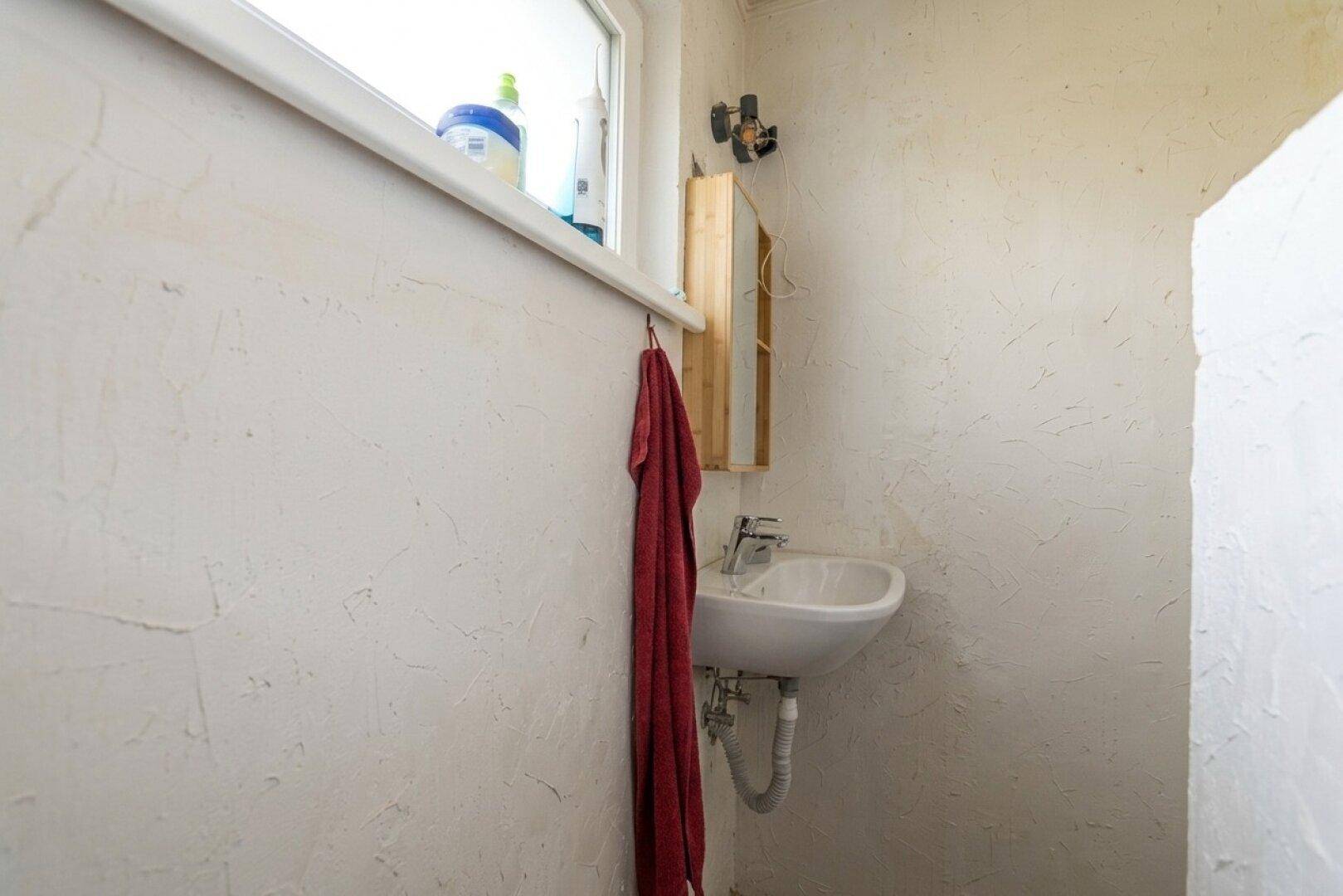 Kleines WC mit Waschbecken und Fenster, hell und funktional gestaltet.