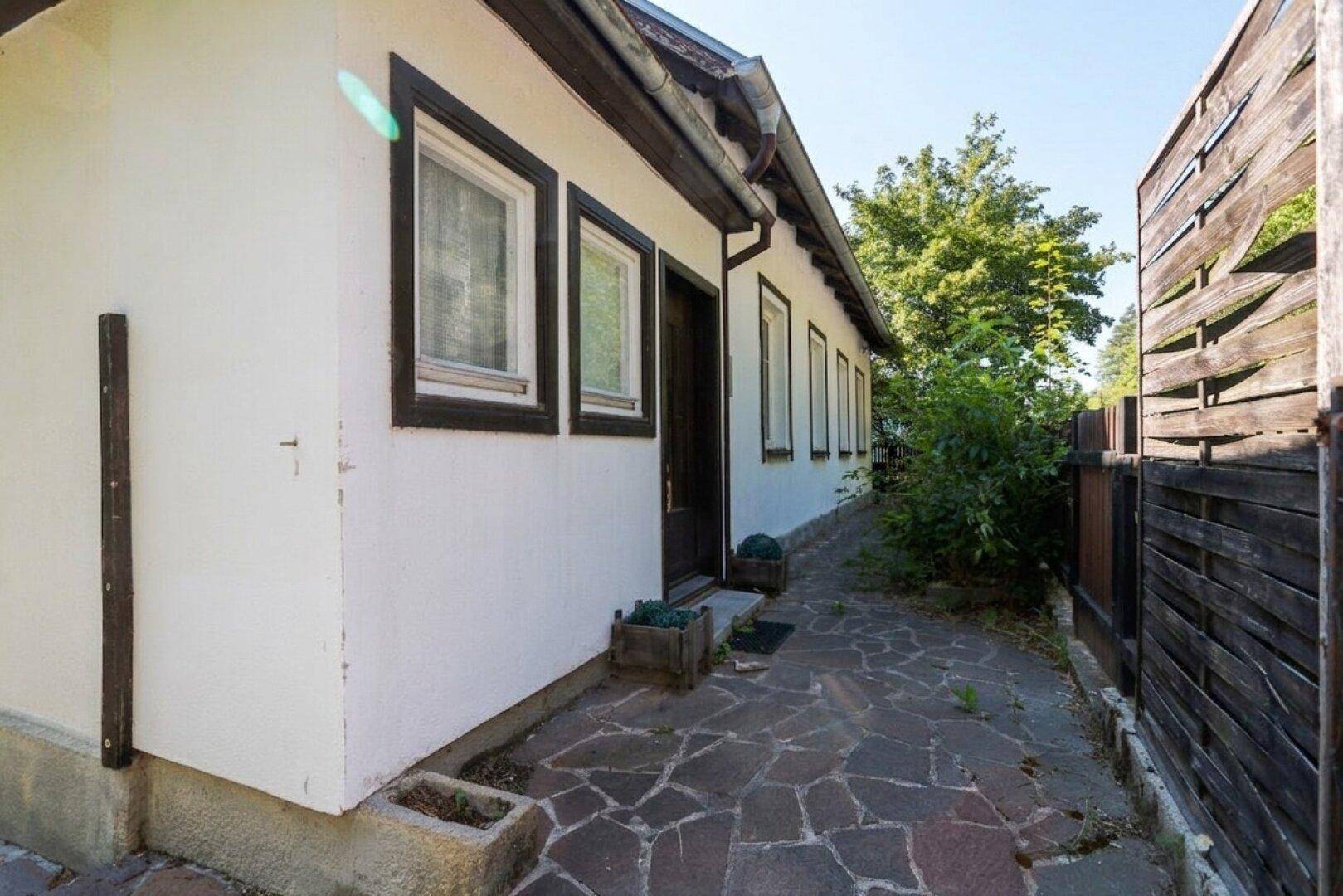 Seitenansicht des Nebengebäudes mit gepflastertem Weg und Holzzaun.
