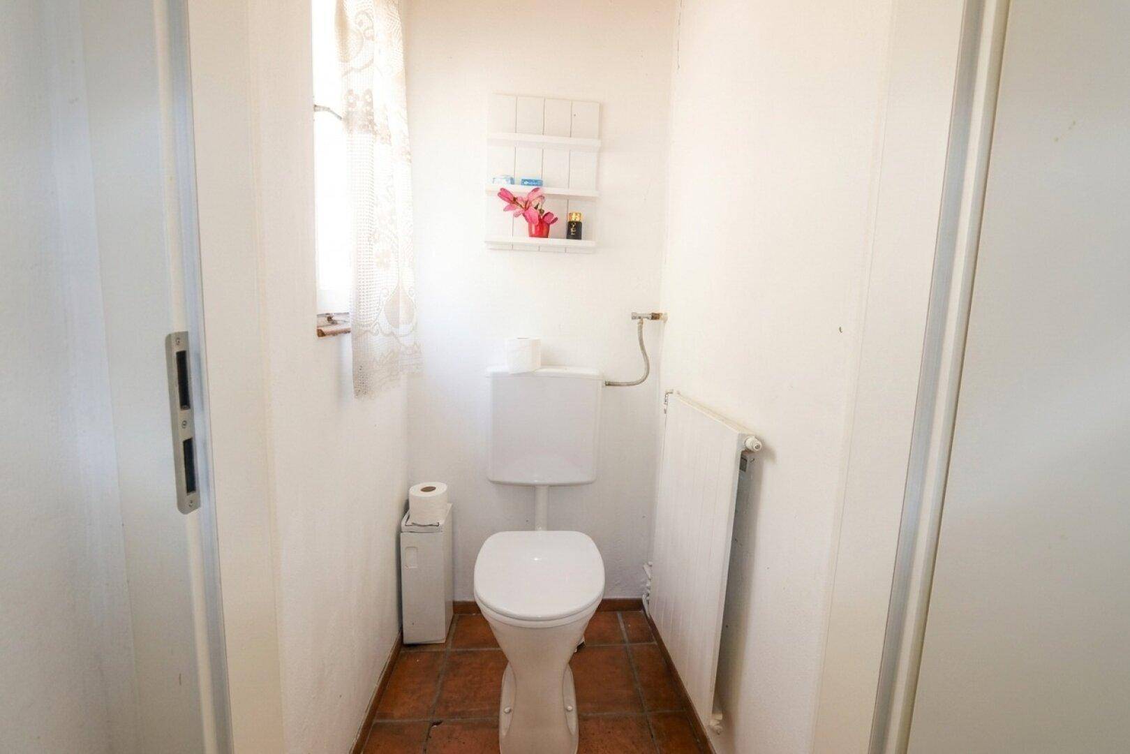 Kleines separates WC mit Fenster und Terrakotta-Fliesenboden.