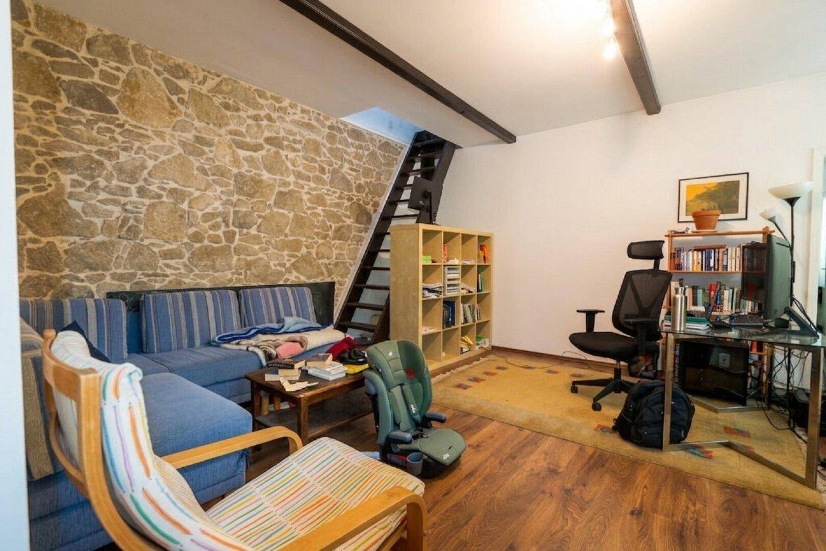 Wohnzimmer mit markanter Steinwand, Holzfußboden und offener Treppe.