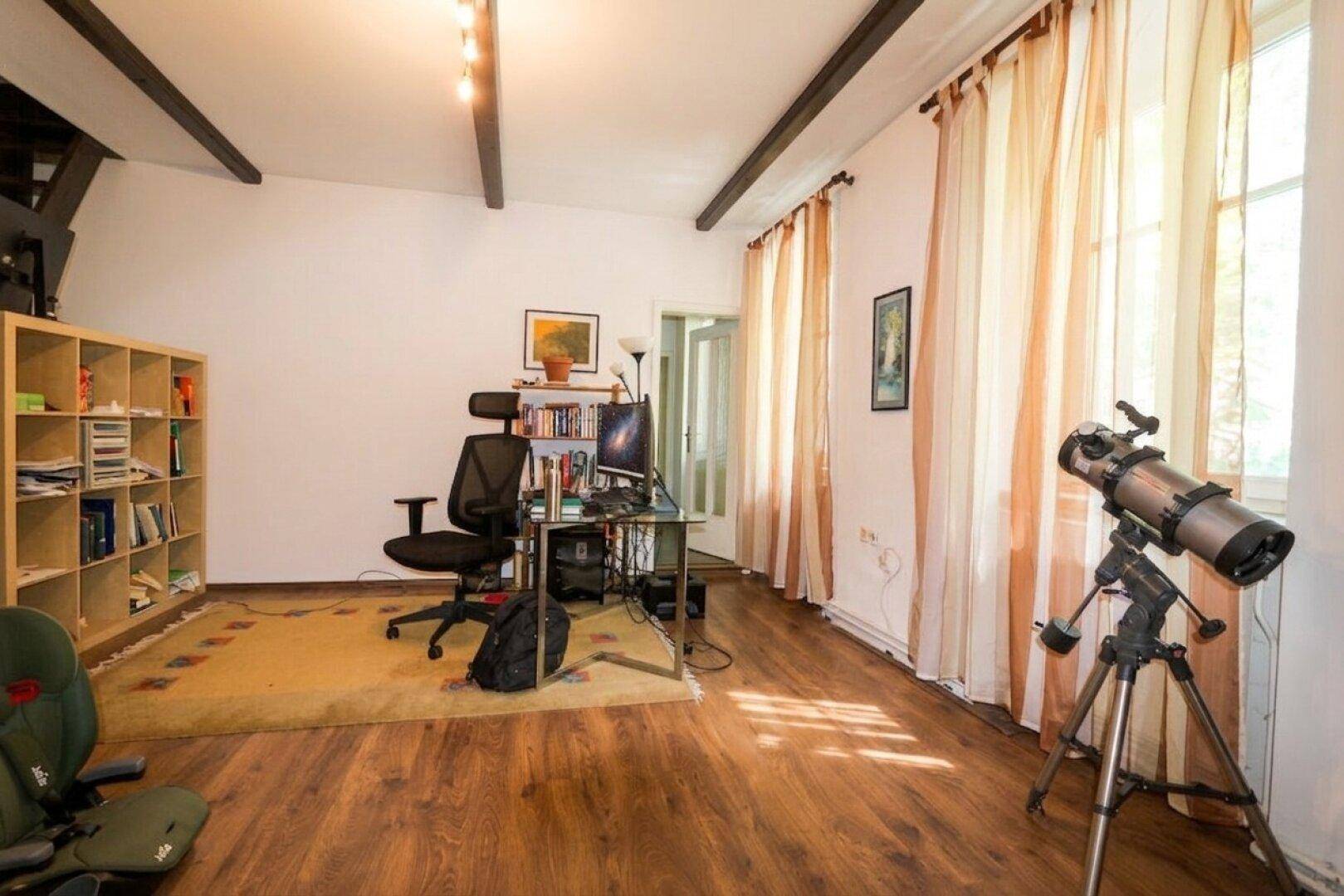 Heller Wohnraum mit Holzfußboden, hohen Decken und einem Teleskop am Fenster.