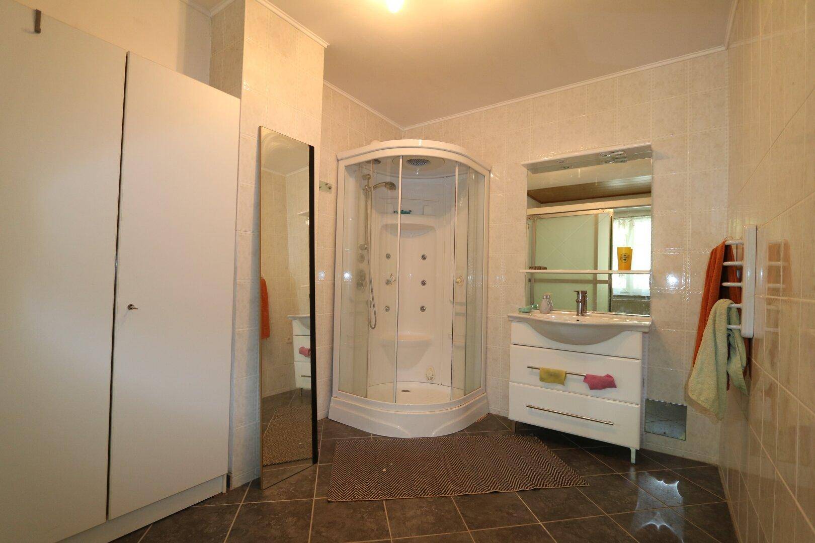 Funktionales Badezimmer mit Duschkabine, Einzelwaschbecken, Spiegelschrank und hellen Fliesen.