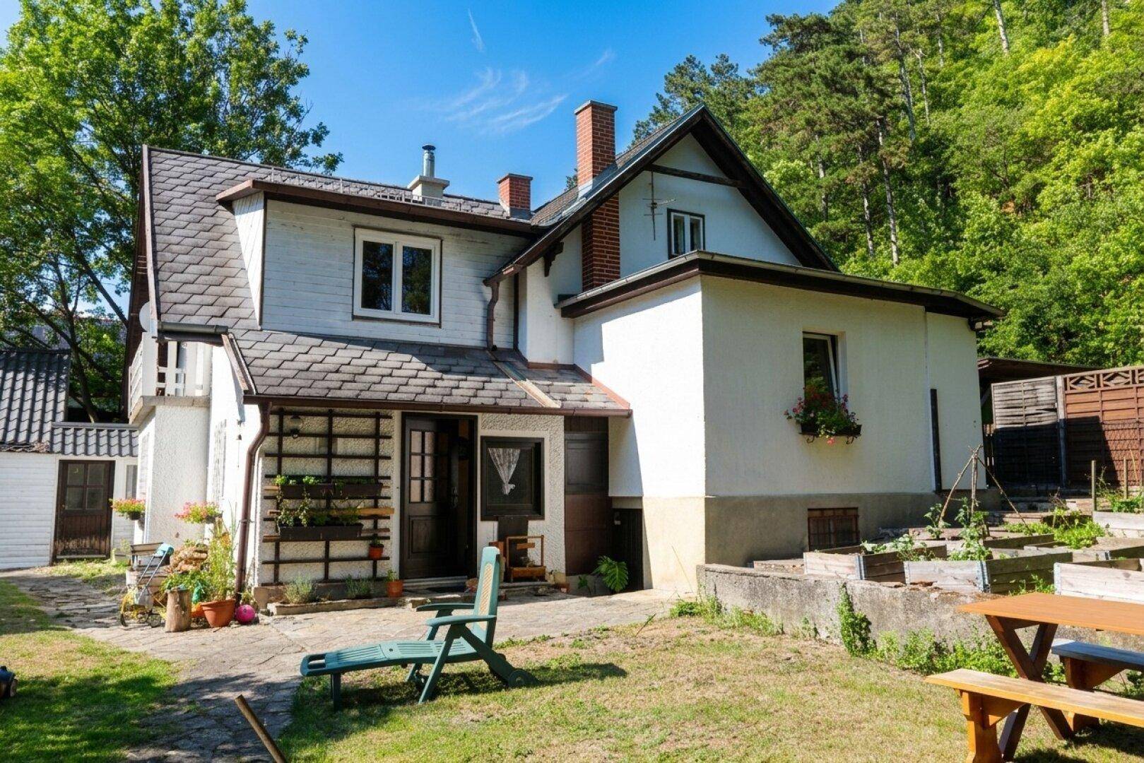 Traditionelles Haus mit Garten, Hochbeeten, Rasenfläche und Sitzgelegenheiten im Freien.