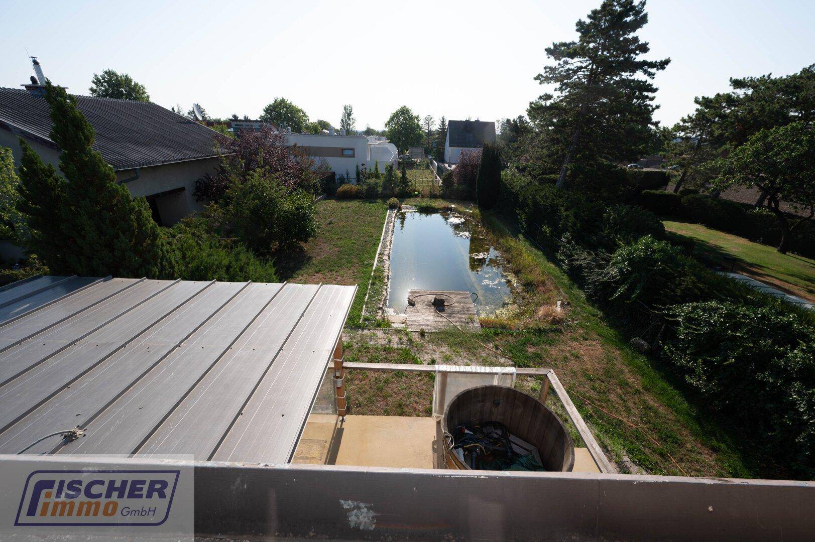 Blick vom Balkon auf den Garten mit Teich und die umliegende Landschaft.