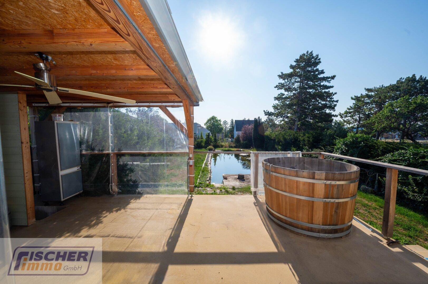 Überdachte Terrasse mit Holz-Whirlpool und weitem Blick auf den Gartenteich und die Umgebung.