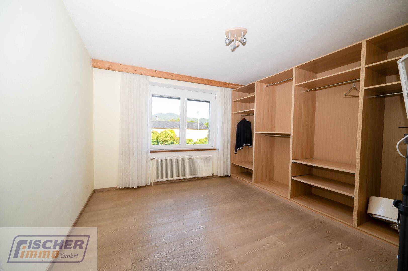 Schlafzimmer mit Einbauschränken, Holzboden und Fenster mit Blick auf die Umgebung.