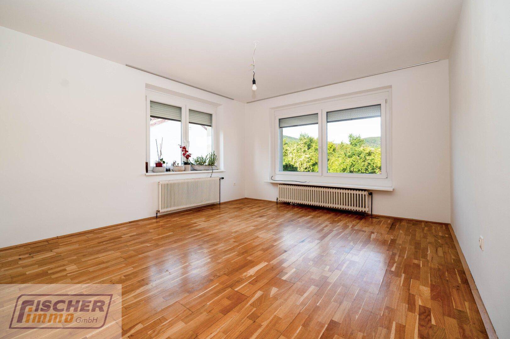 Helles Zimmer mit Parkettboden, großen Fenstern und Blick ins Grüne.