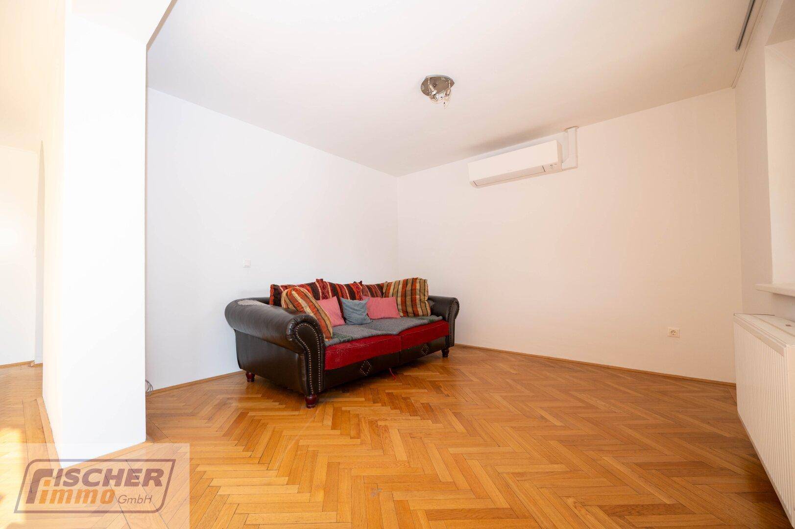 Geräumiges Wohnzimmer mit Parkettboden, Klimaanlage und gemütlichem Sofa.