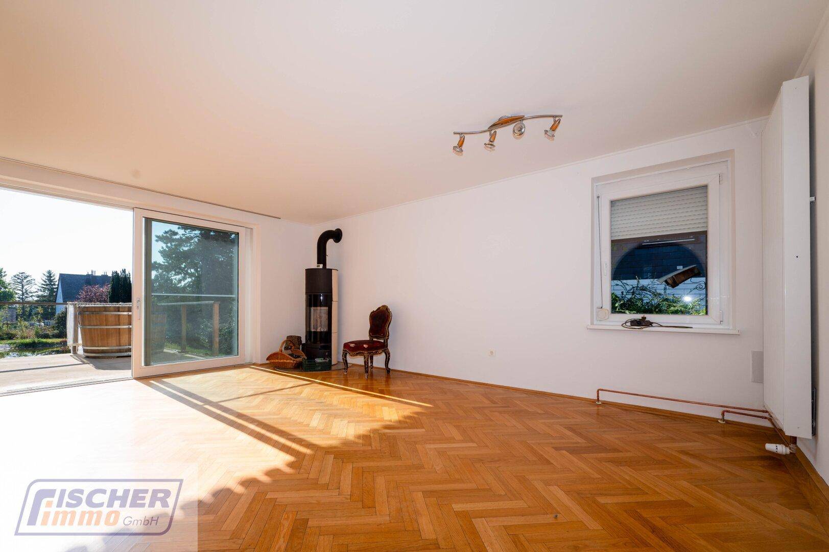 Lichtdurchflutetes Wohnzimmer mit Kaminofen, Parkettboden und Schiebetür zur Terrasse.