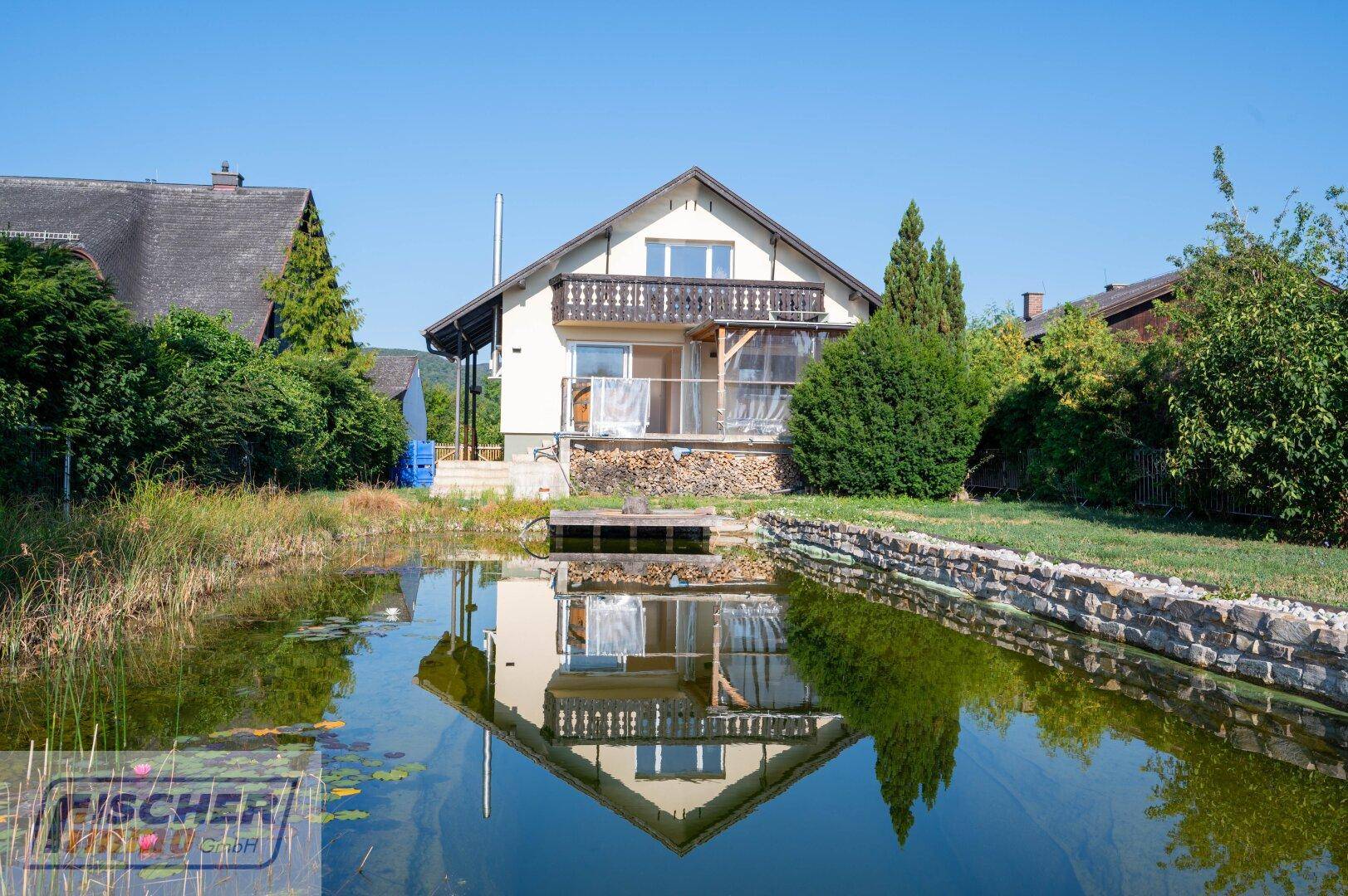 Malerischer Garten mit Teich, der das Haus und den blauen Himmel spiegelt.