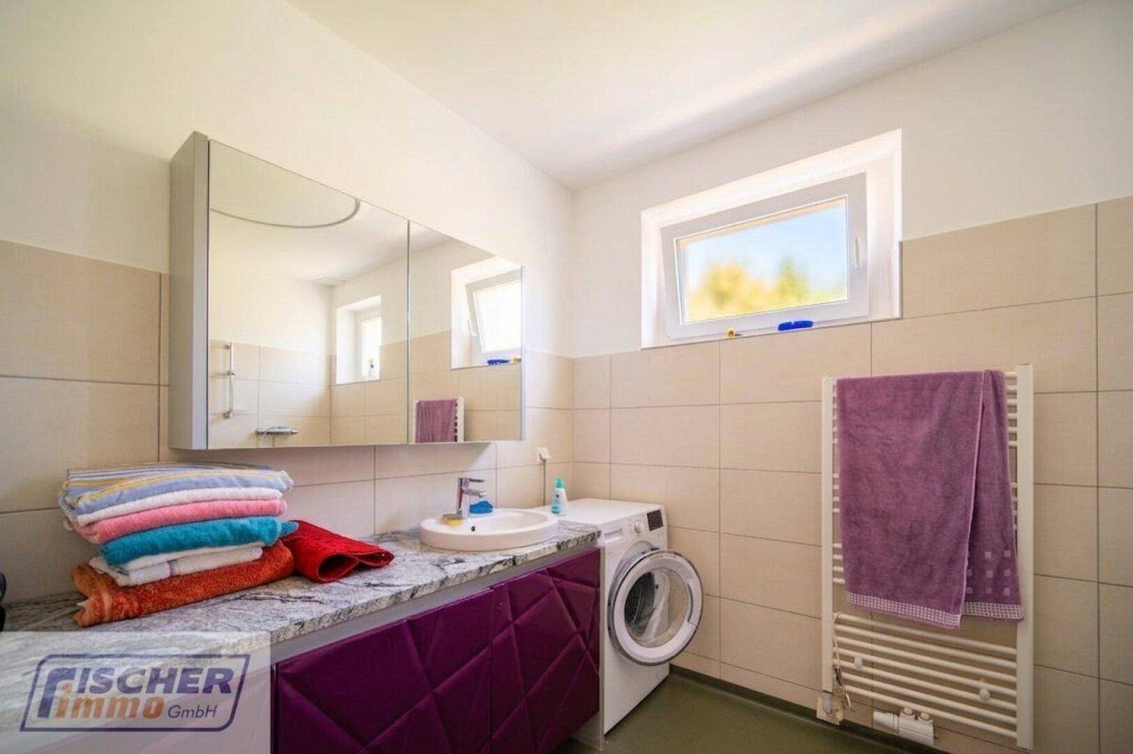 Badezimmer mit Einzelwaschbecken, Spiegelschrank, Waschmaschine und Fenster.