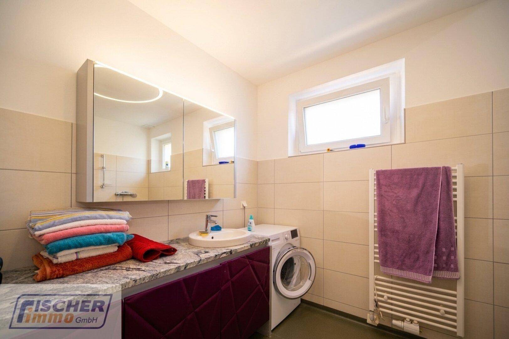 Helles Badezimmer mit Fliesen, Einzelwaschbecken, Spiegelschrank und Waschmaschine.
