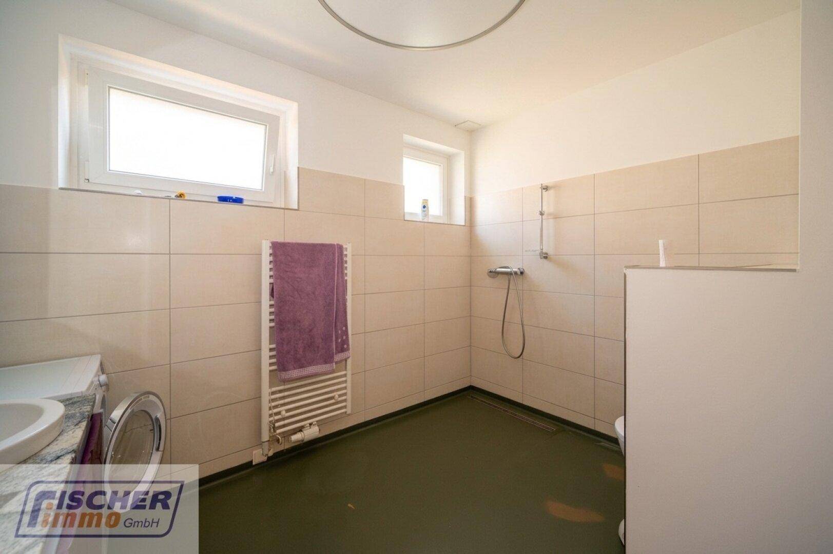 Geräumiges Badezimmer mit beigen Fliesen, Dusche und Fenster für Tageslicht.