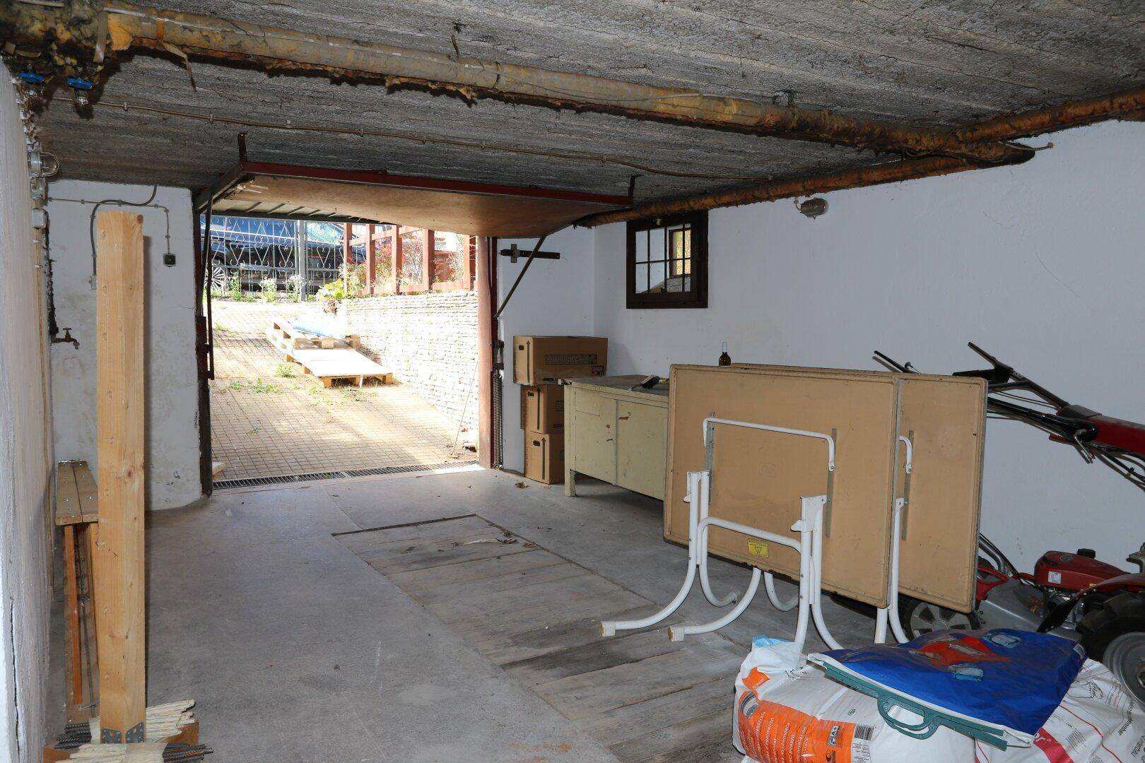 Geräumige Garage im Untergeschoss mit Betonboden, kleinem Fenster und direktem Zugang nach draußen.