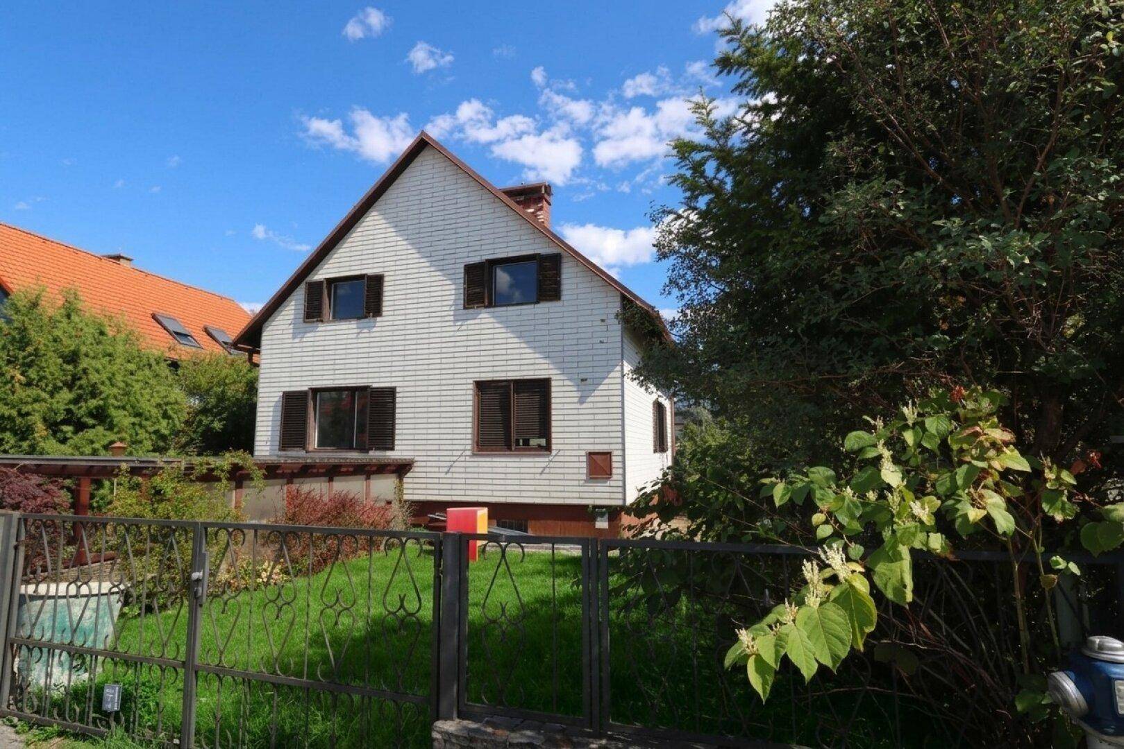 Rückansicht des Hauses mit weißer Holzverkleidung, Fensterläden und einem umzäunten Vorgarten.