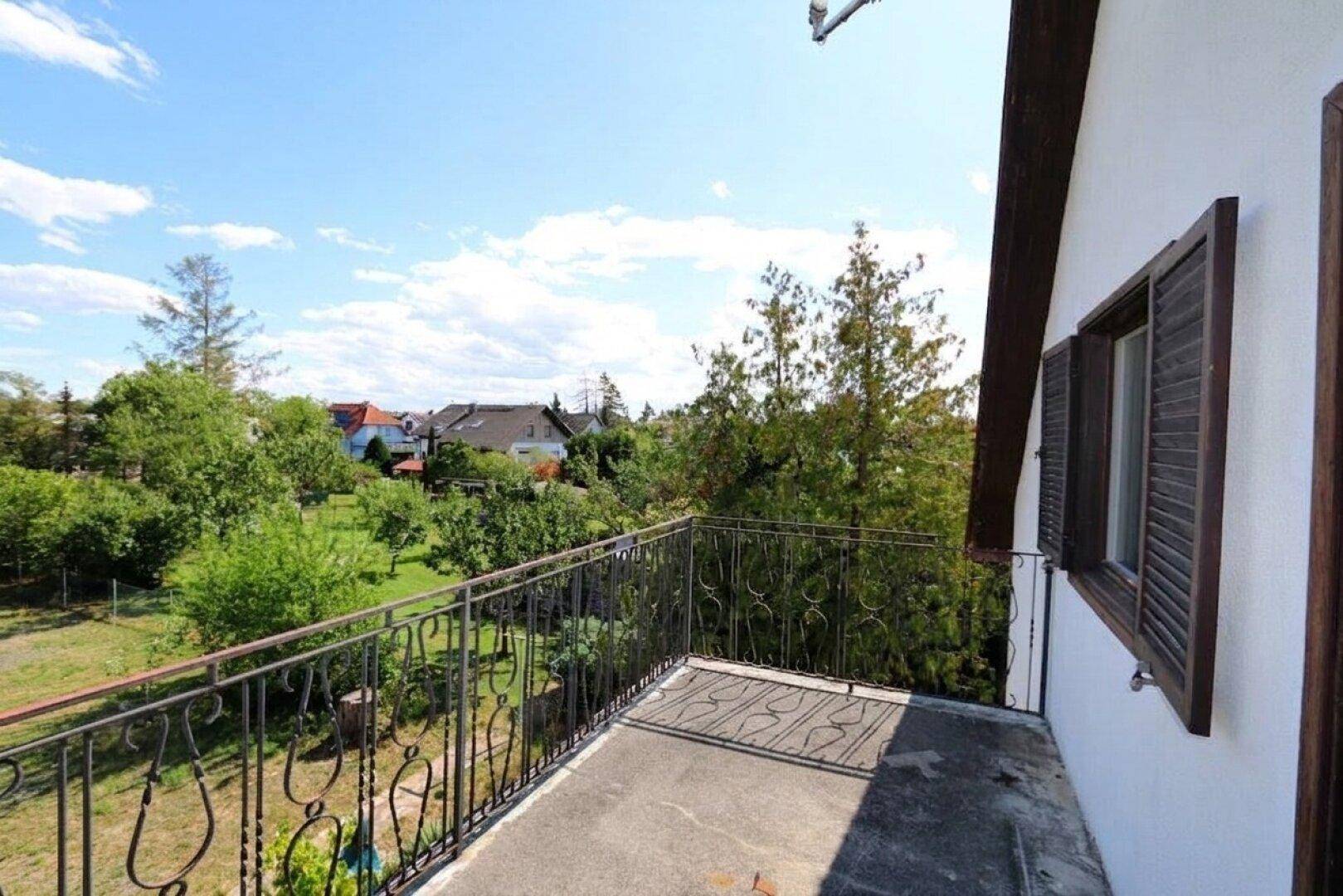 Balkon mit schmiedeeisernem Geländer und weitem Blick über den grünen Garten und die Umgebung.