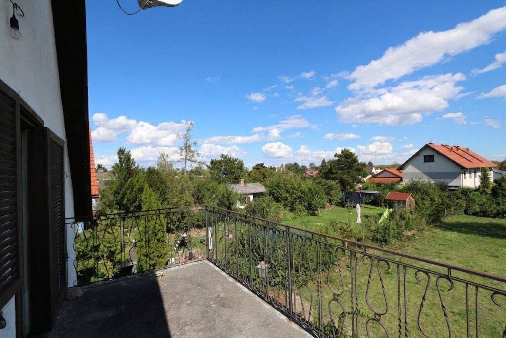 Balkon mit Blick auf die umliegende Landschaft und weitere Häuser unter blauem Himmel.
