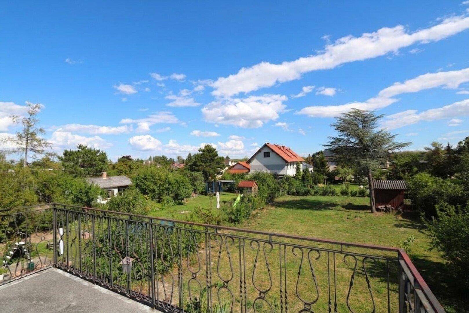 Balkon mit weitem Blick über den Garten, Bäume und die ländliche Umgebung an einem sonnigen Tag.