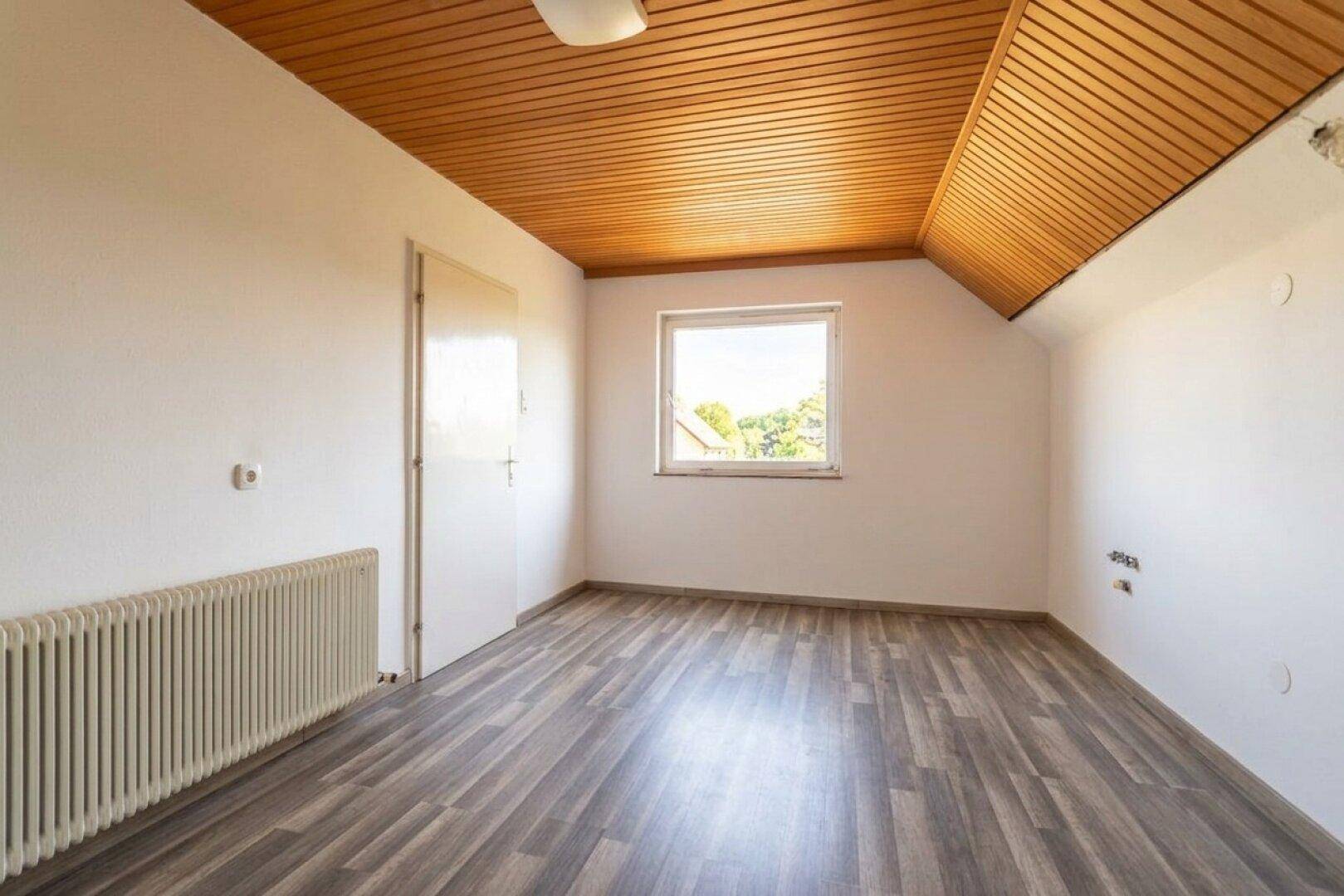 Geräumiges Schlafzimmer im Dachgeschoss mit Laminatboden, Holzdecke und Heizkörper.