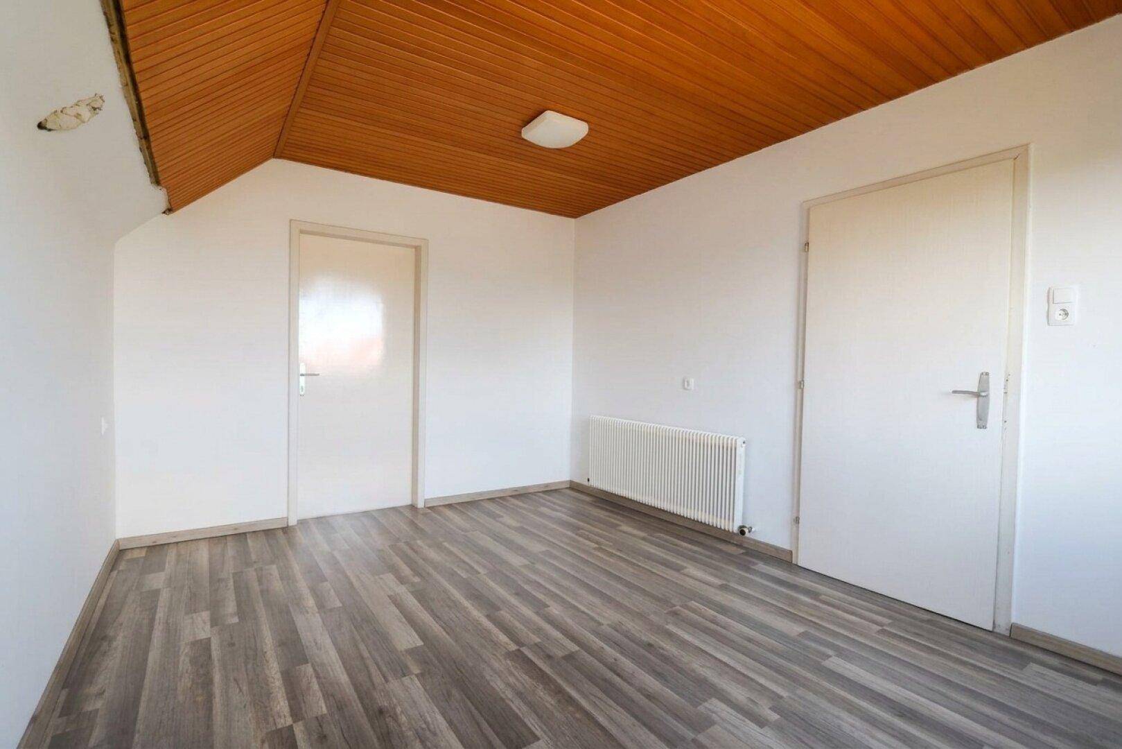 Schlafzimmer im Dachgeschoss mit Laminatboden, Holzdecke und zwei Türen.