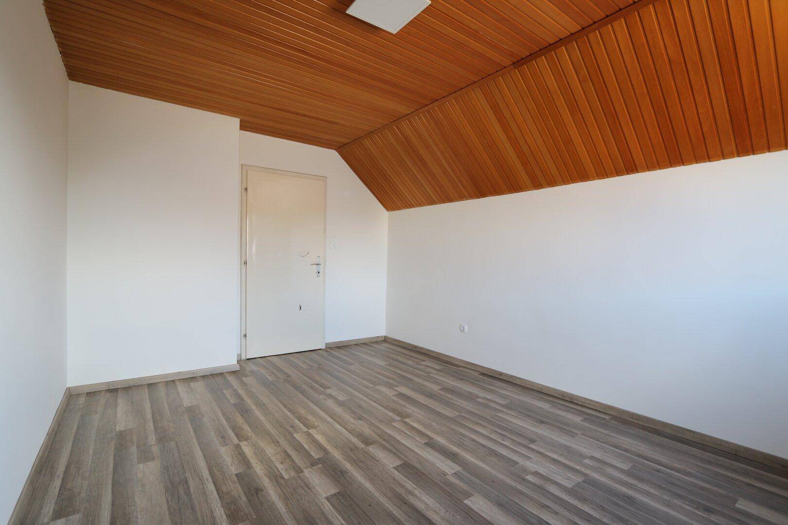 Schlafzimmer im Dachgeschoss mit Laminatboden, Holzdecke und einer Tür.