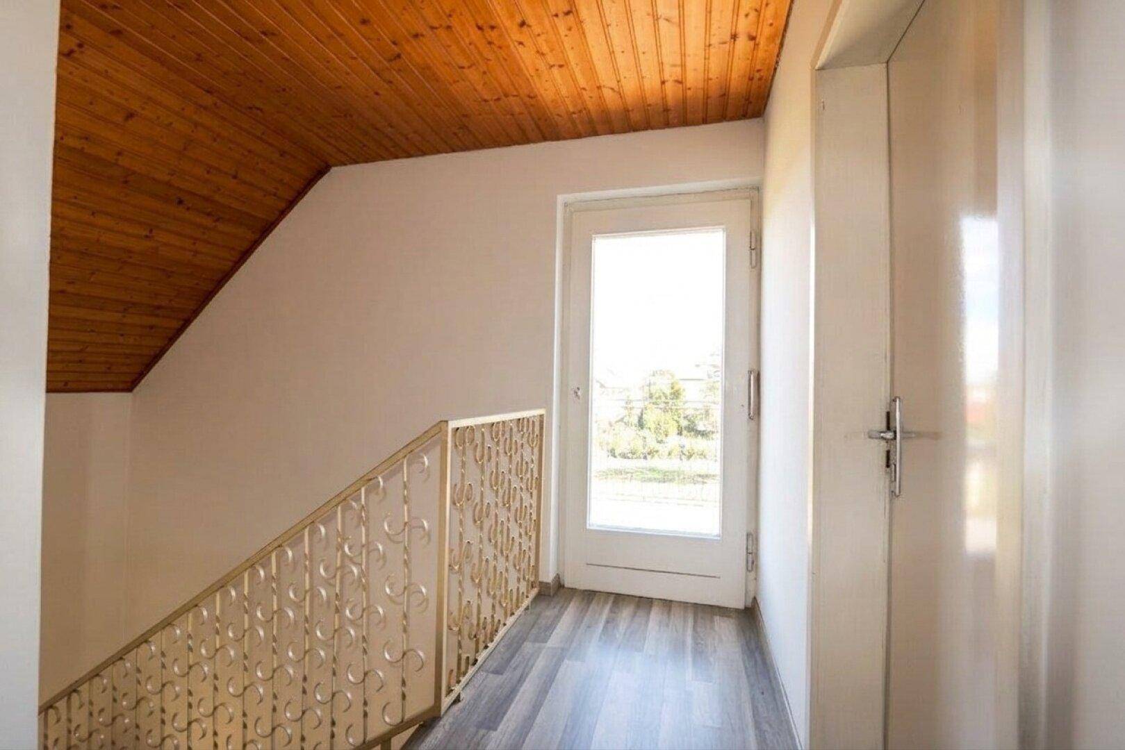 Obergeschossflur mit Laminatboden, Holzdecke und einer Tür, die auf den Balkon führt.