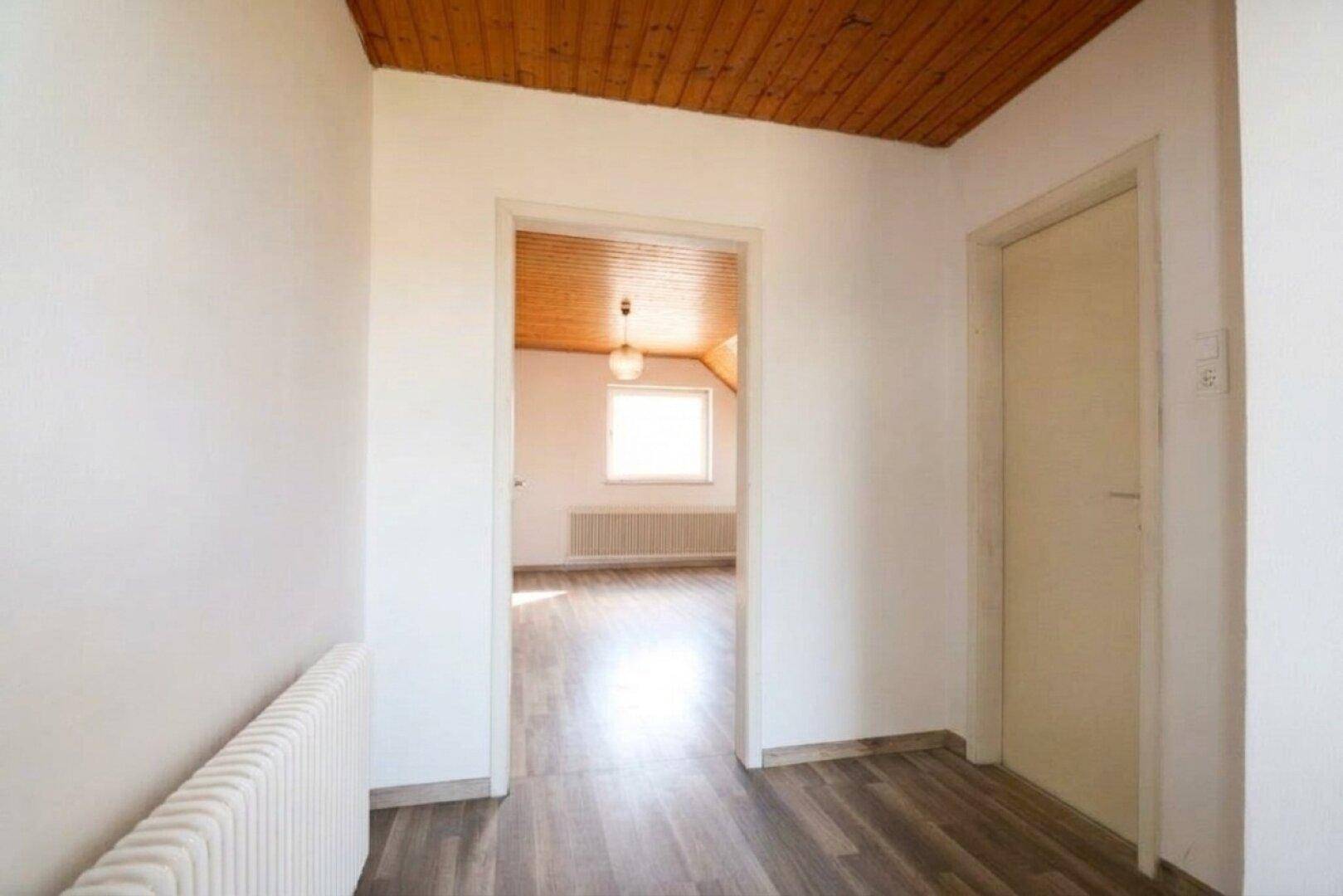 Heller Flur im Obergeschoss mit Laminatboden, Holzdecke und Blick in ein weiteres Zimmer.
