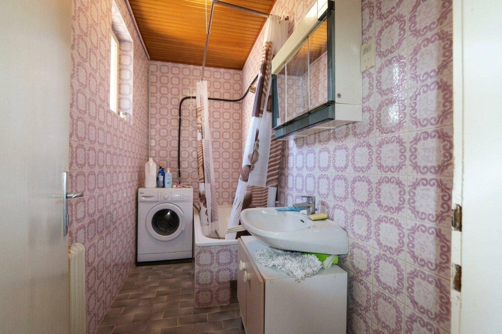 Badezimmer mit rosa gemusterten Fliesen, Holzdecke und einer Badewanne mit Duschvorhang.