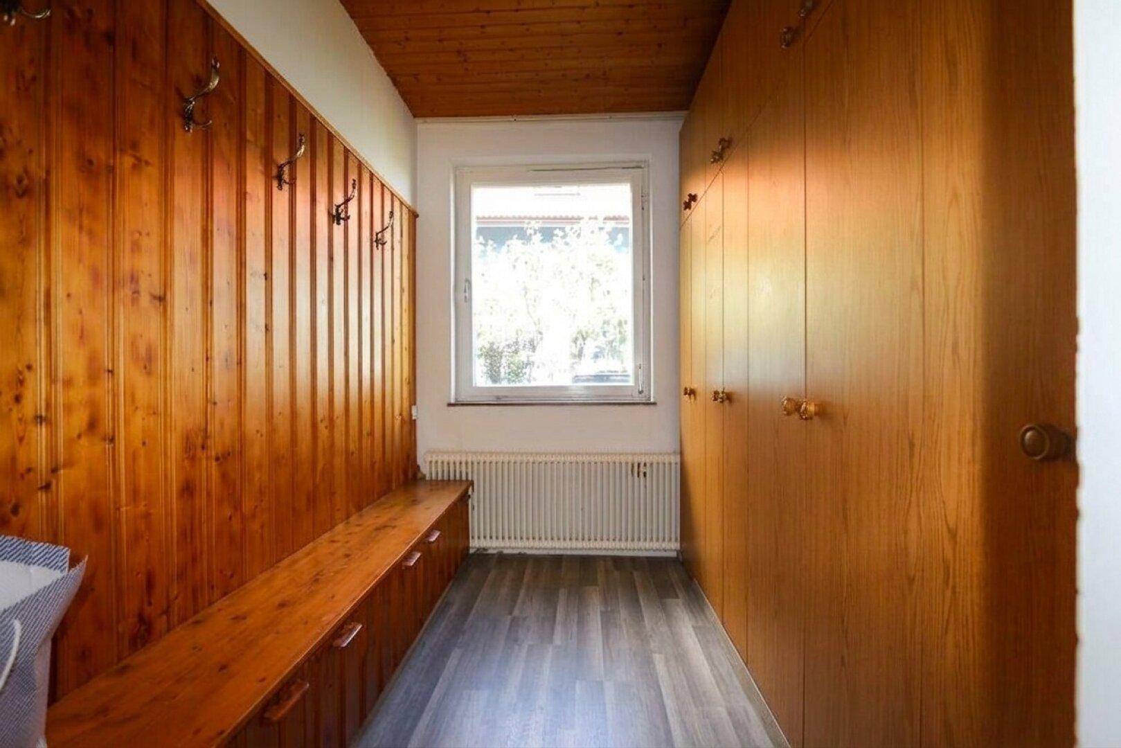 Flur mit Holzvertäfelung, Einbauschränken und einem Fenster, das den Raum erhellt.