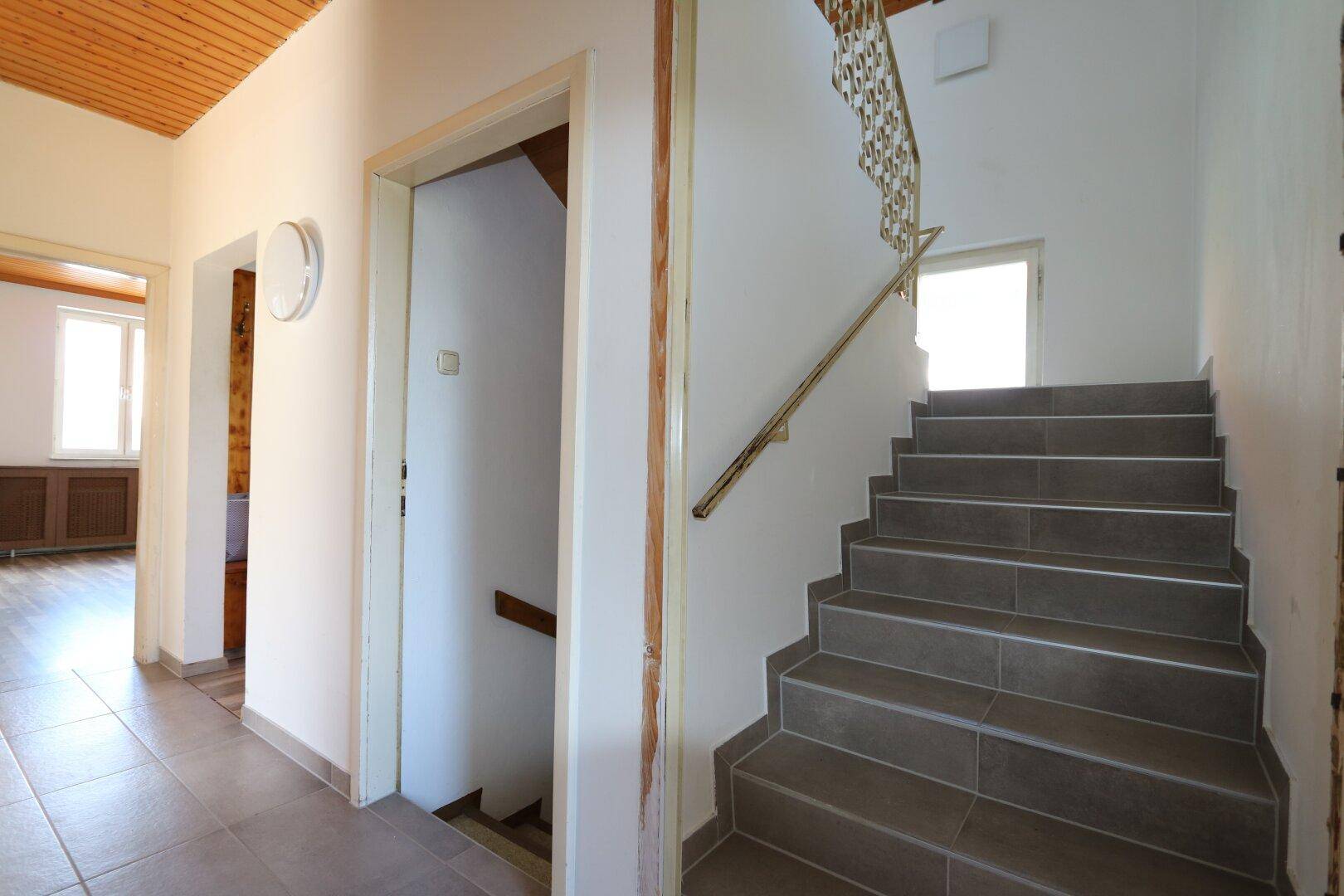 Flur mit gefliestem Boden, Holzdecke und einer Treppe zum Obergeschoss mit schmiedeeisernem Geländer.