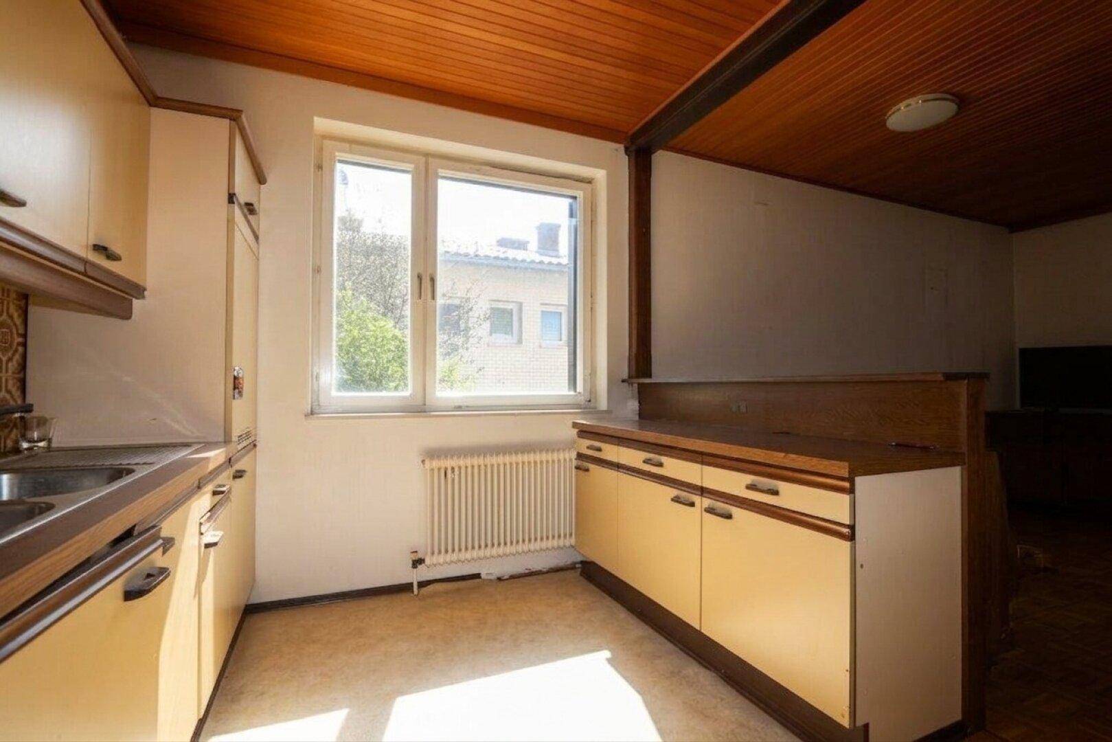 Küchenbereich mit Fenster, Heizkörper und einer Theke, die den Raum optisch abtrennt.