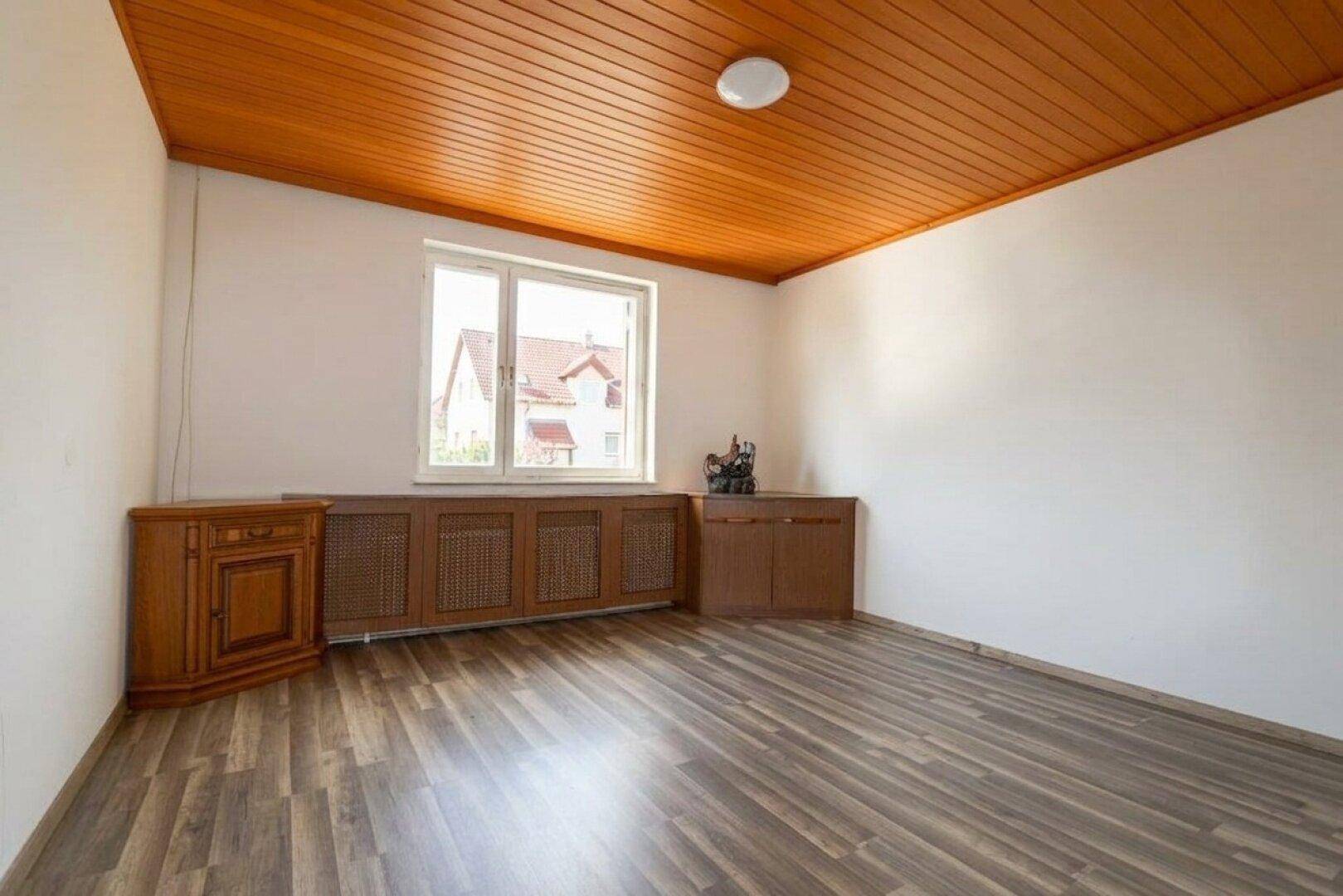Schlafzimmer mit Laminatboden, Holzdecke und einem Fenster, das viel Tageslicht hereinlässt.