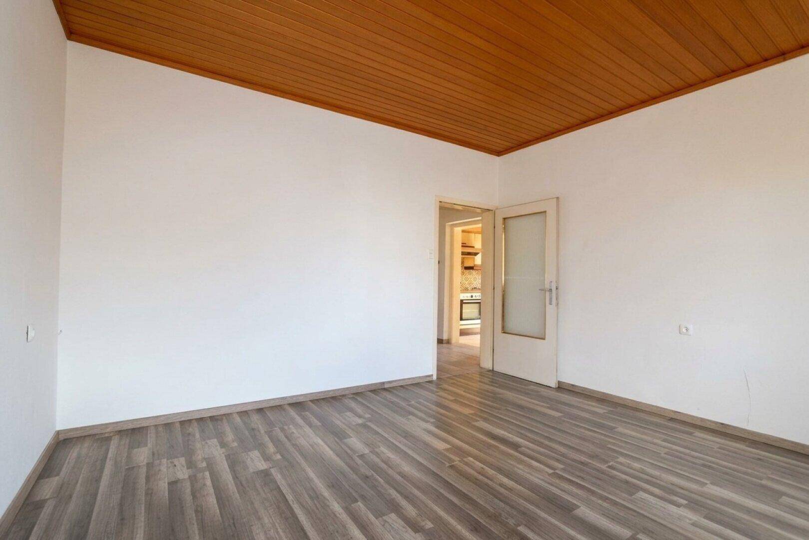 Helles Schlafzimmer mit Laminatboden, Holzdecke und einer Tür, die in einen anderen Raum führt.