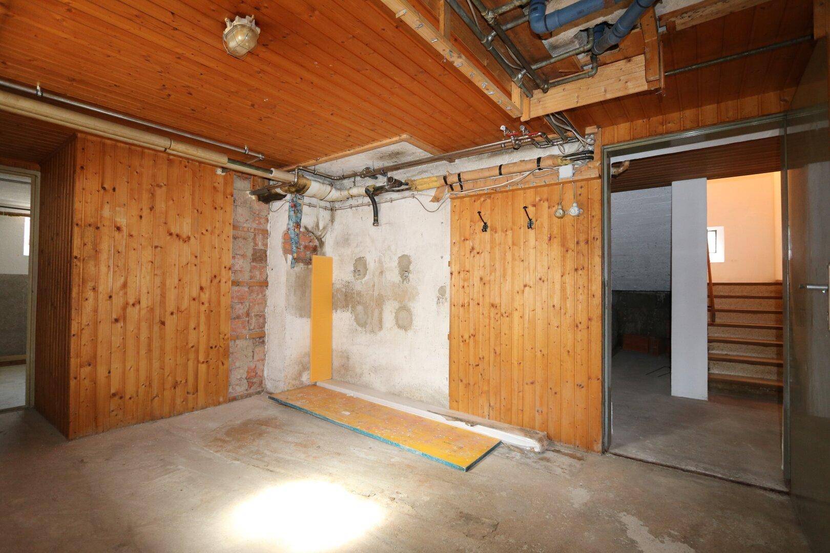 Kellerraum mit Holzverkleidung an den Wänden, Betonboden und sichtbaren Deckeninstallationen und Rohren.
